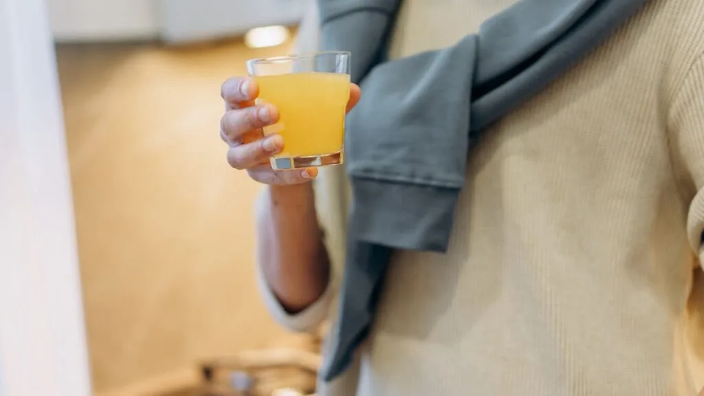 Person holding a glass of orange juice in a kitchen — synbiotic supplement morning routine