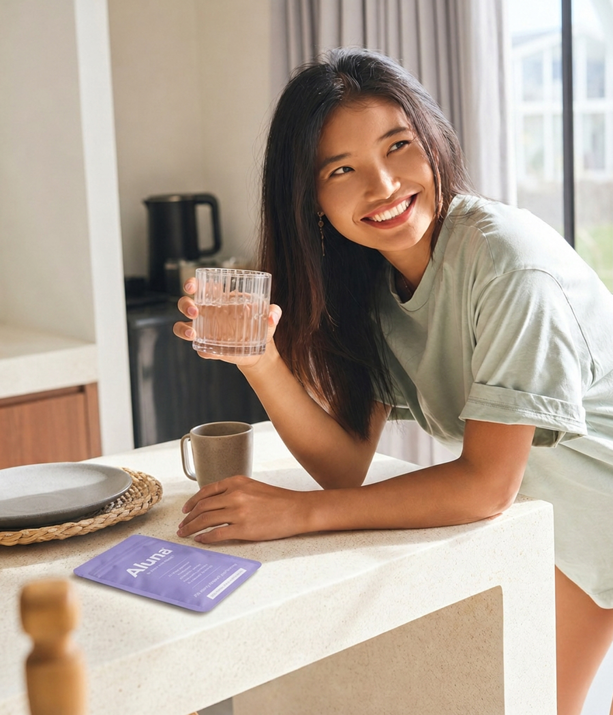 Smiling woman with a glass of water and an Aluna pouch